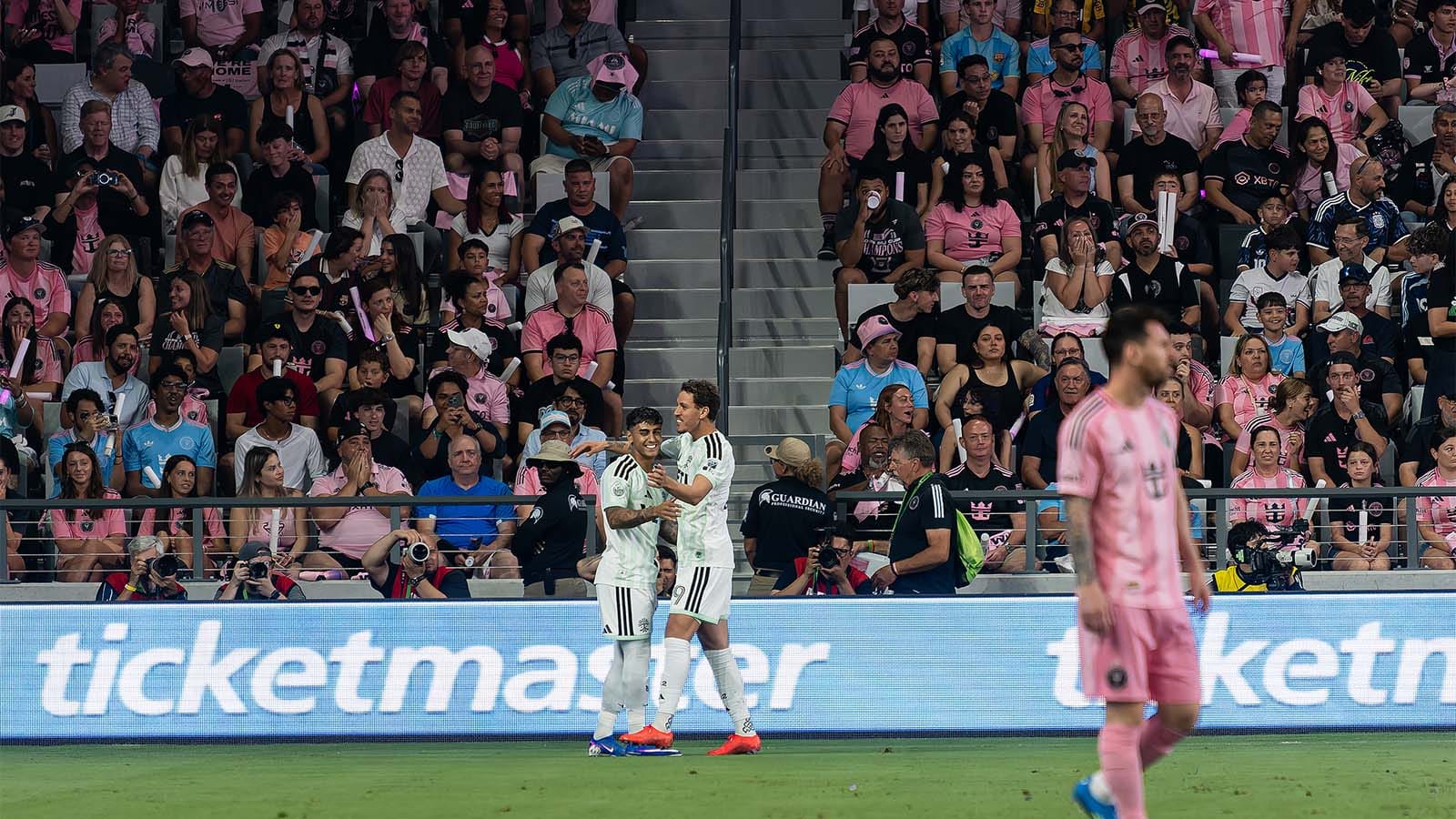 Facundo Torres and Guilherme Biro of Austin FC celebrating goal while Lionel Messi is grumpy in foreground and Miami fans are shocked in background