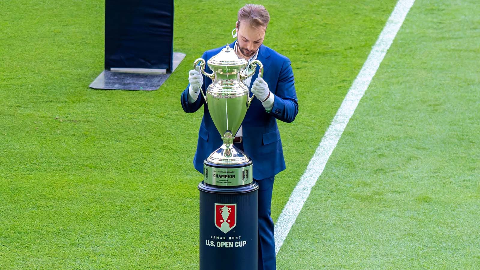 Official in suit wearing gloves putting U.S. Open Cup trophy on branded stand